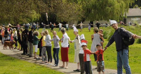 Part of a large circle of people, of all ages stood together holding hands.