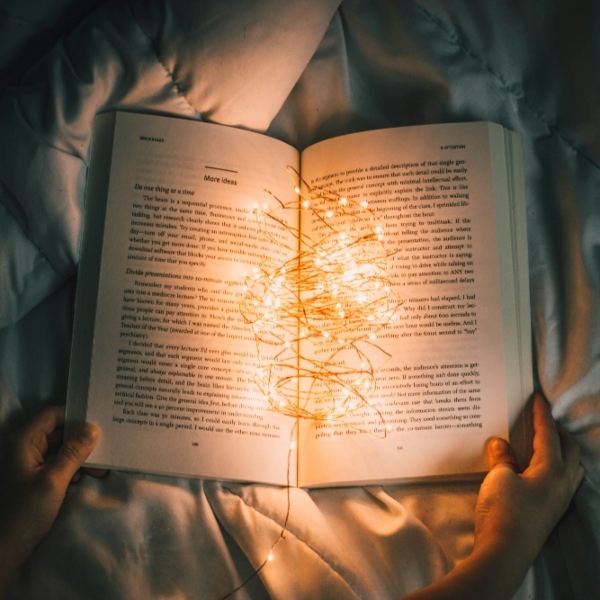 Hans hold open a book underneath some bedsheets. It's lit by string of tiny lights resting on the open pages.