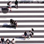 Looking down on a black and white striped walkway with groups of people walking across.
