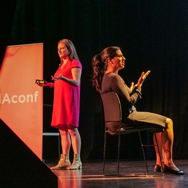 Cath Hume, AMA's CEO stands on a stage. A BSL interpreter sits next to her.