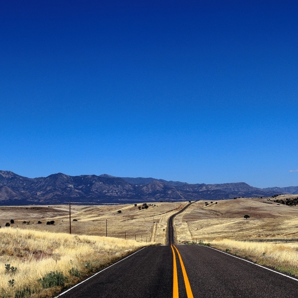 A road reaches out to the horizon under a bright, cloudless sky.