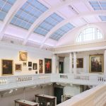 Interior of Cornwall Museum with impressive glass atrium ceiling and paintings surrounding the balcony.