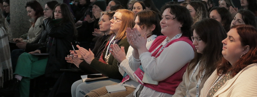 A packed auditorium with people clapping. 