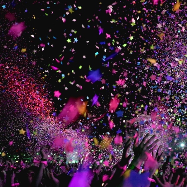 A large crowd celebrating at night. The sky is full of bursts of colourful paper cascading over the crowd.