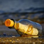 A glass bottle on the seashore with a message curled on paper inside it.